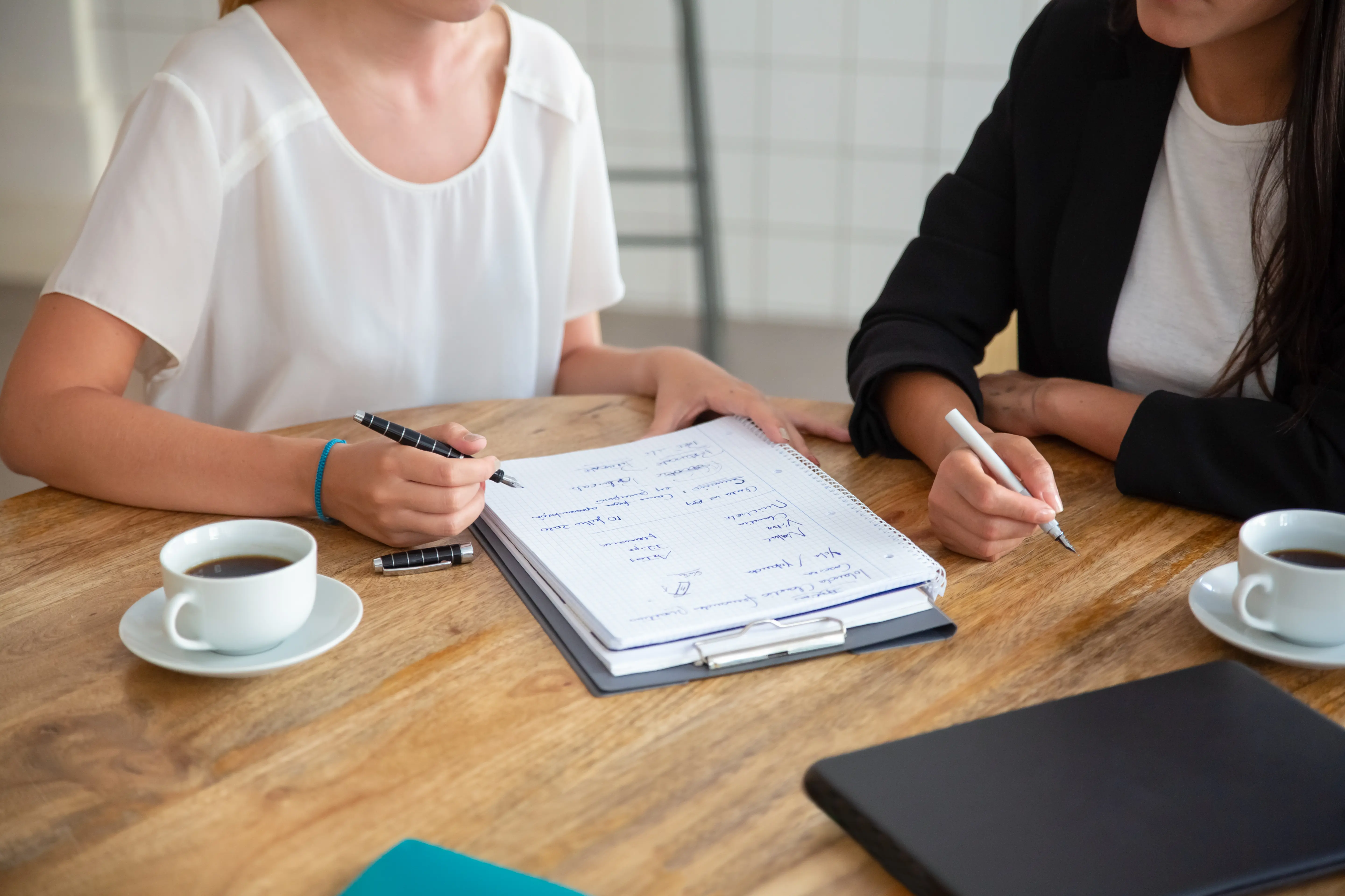 Two women discussing ideas while taking notes