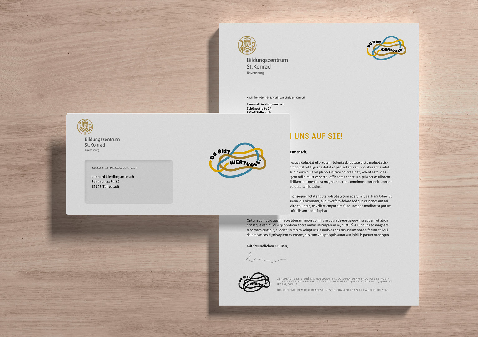 Briefbogen und Briefumschlag des Bildungszentrums St. Konrad mit Logos und Briefadresse auf hellem Holztisch.