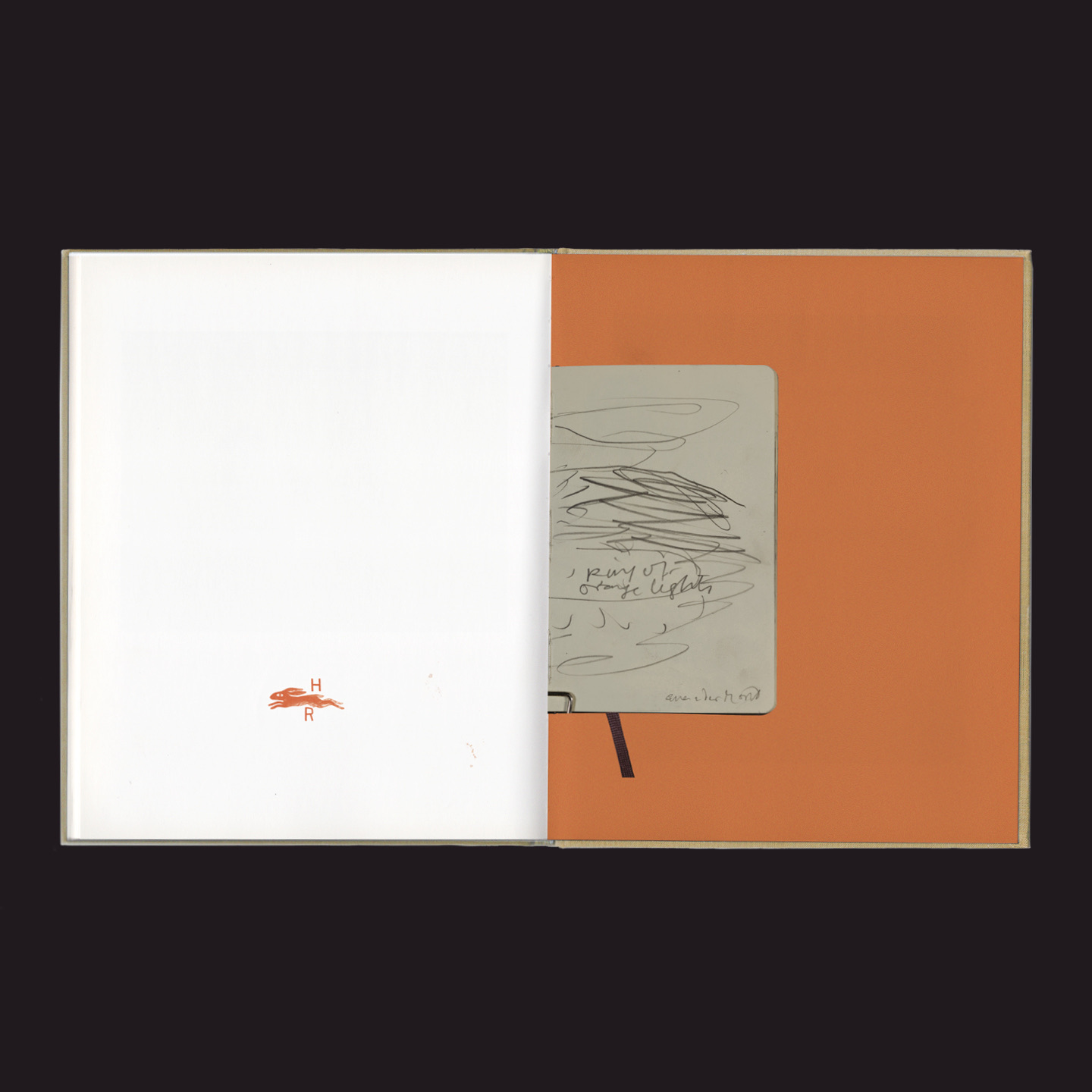 Geöffnetes Buch mit linker weißer Seite und kleinem roten Logo, rechte Seite orange mit einer befestigten, handschriftlich mit Kritzeleien und Notizen versehene beige Karte.