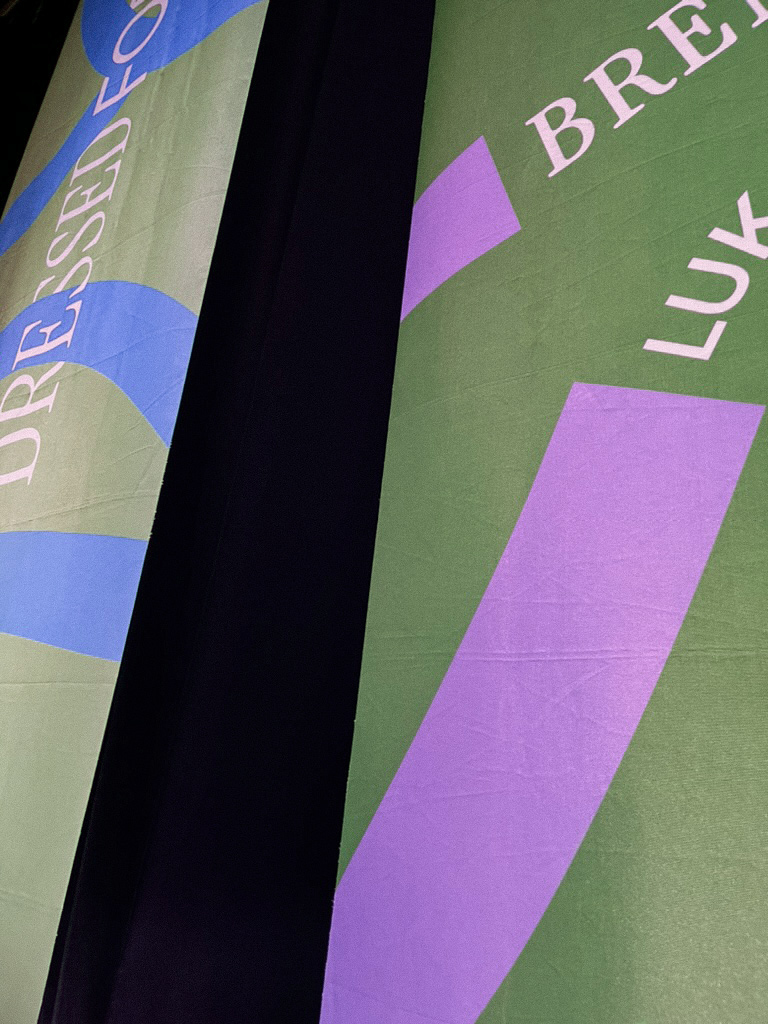 Nahaufnahme von bunten Stoffbahnen mit Texten und geometrischen Mustern in Blau, Lila und Grün, getrennt durch einen schwarzen Streifen.