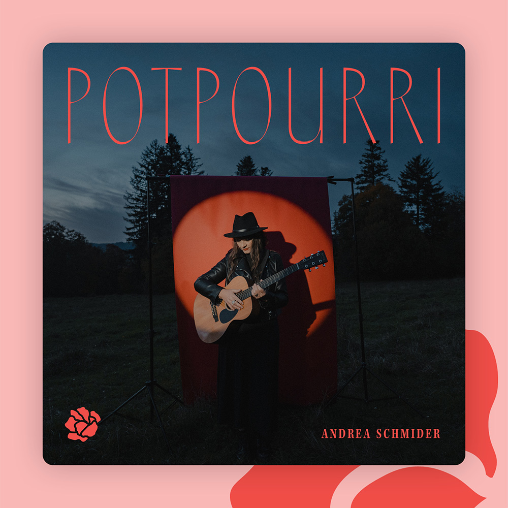 Andrea Schmider spielt Gitarre vor rotem Hintergrund mit orangefarbenem Spot, umgeben von Bäumen im Dämmerlicht.