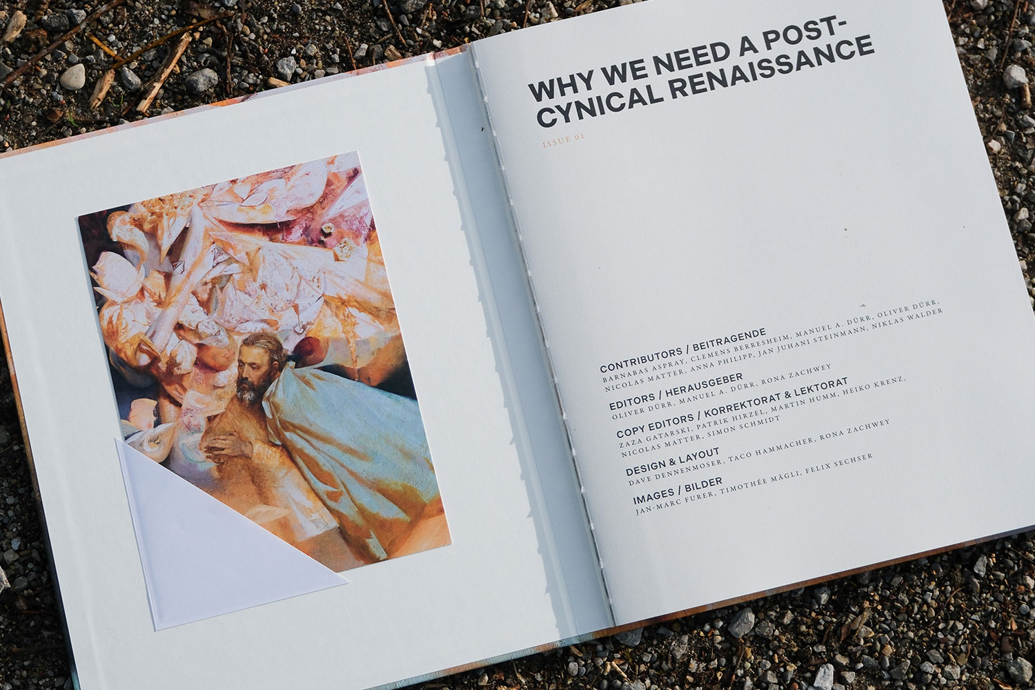 Foto eines aufgeschlagenen Buchs mit Architekturtext und Bild, auf einem erdigen, mit Moos bedeckten Boden liegend.