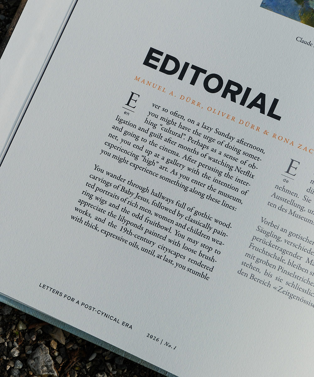 Foto eines aufgeschlagenen Buchs mit Architekturtext und Bild, auf einem erdigen, mit Moos bedeckten Boden liegend.