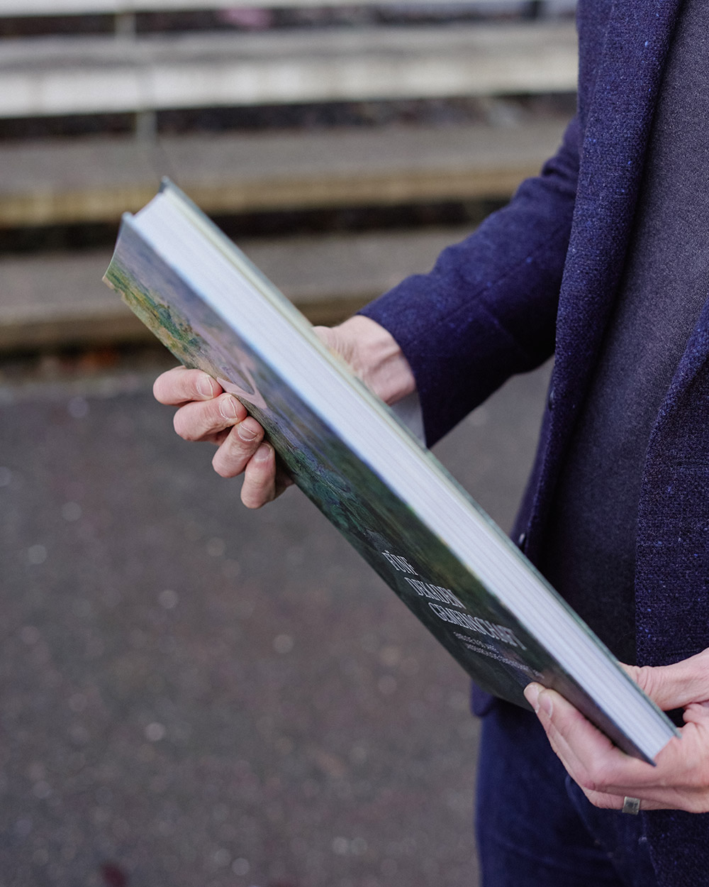 Person hält ein aufgeschlagenes Buch mit grünem Einband in der Hand.