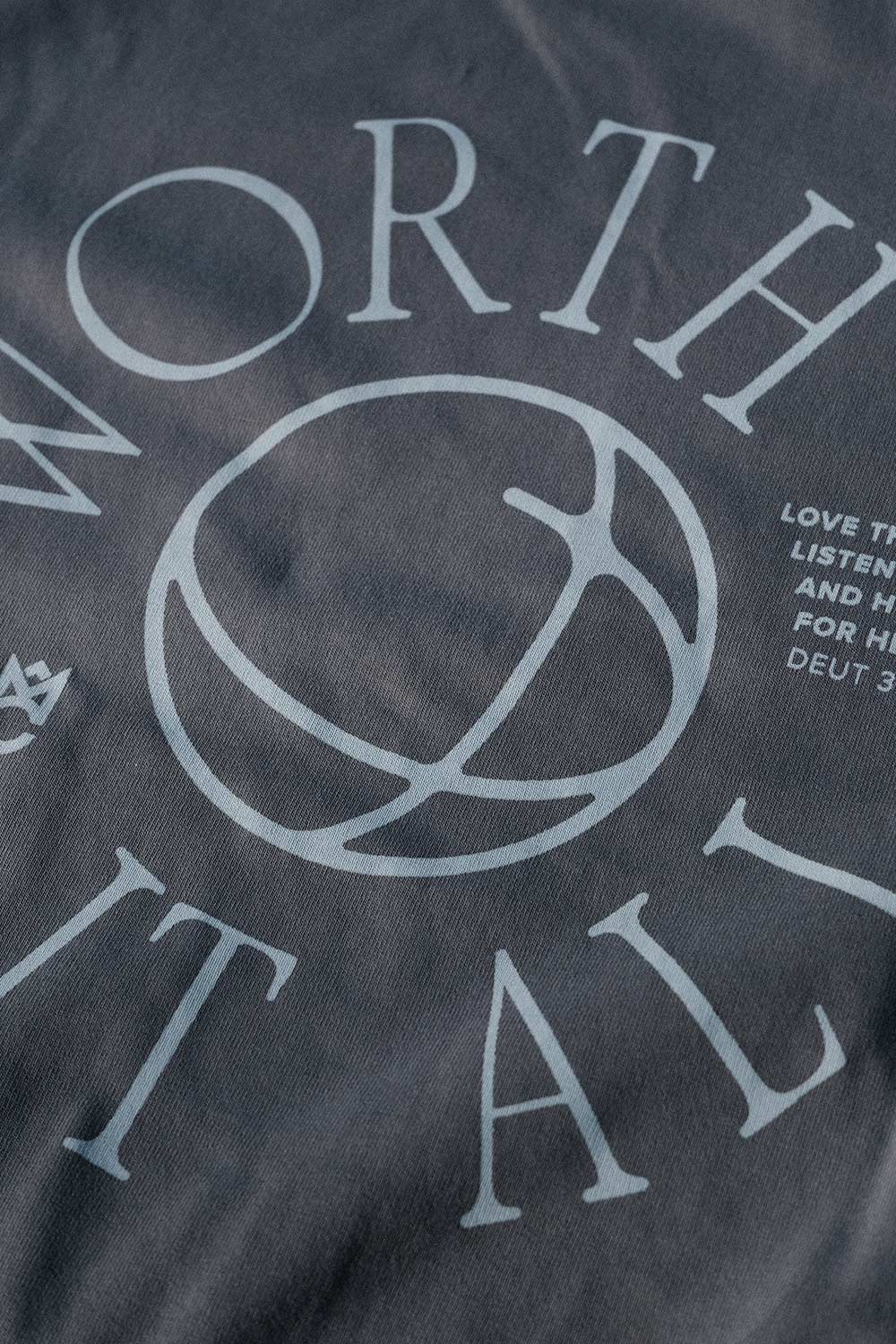 Detaillierte Nahaufnahme eines Shirts mit kreisförmigem Logo und Schriftzug 'WORTH IT ALL'.