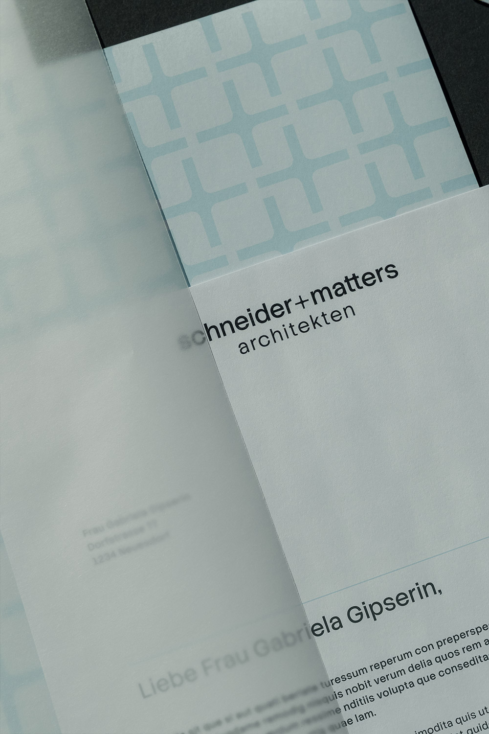 Briefpapier mit dem Logo von schneider+matters architekten, das auf weißen Papier mit dezentem hellblauem Muster zu sehen ist, teilweise von Transparentpapier bedeckt.