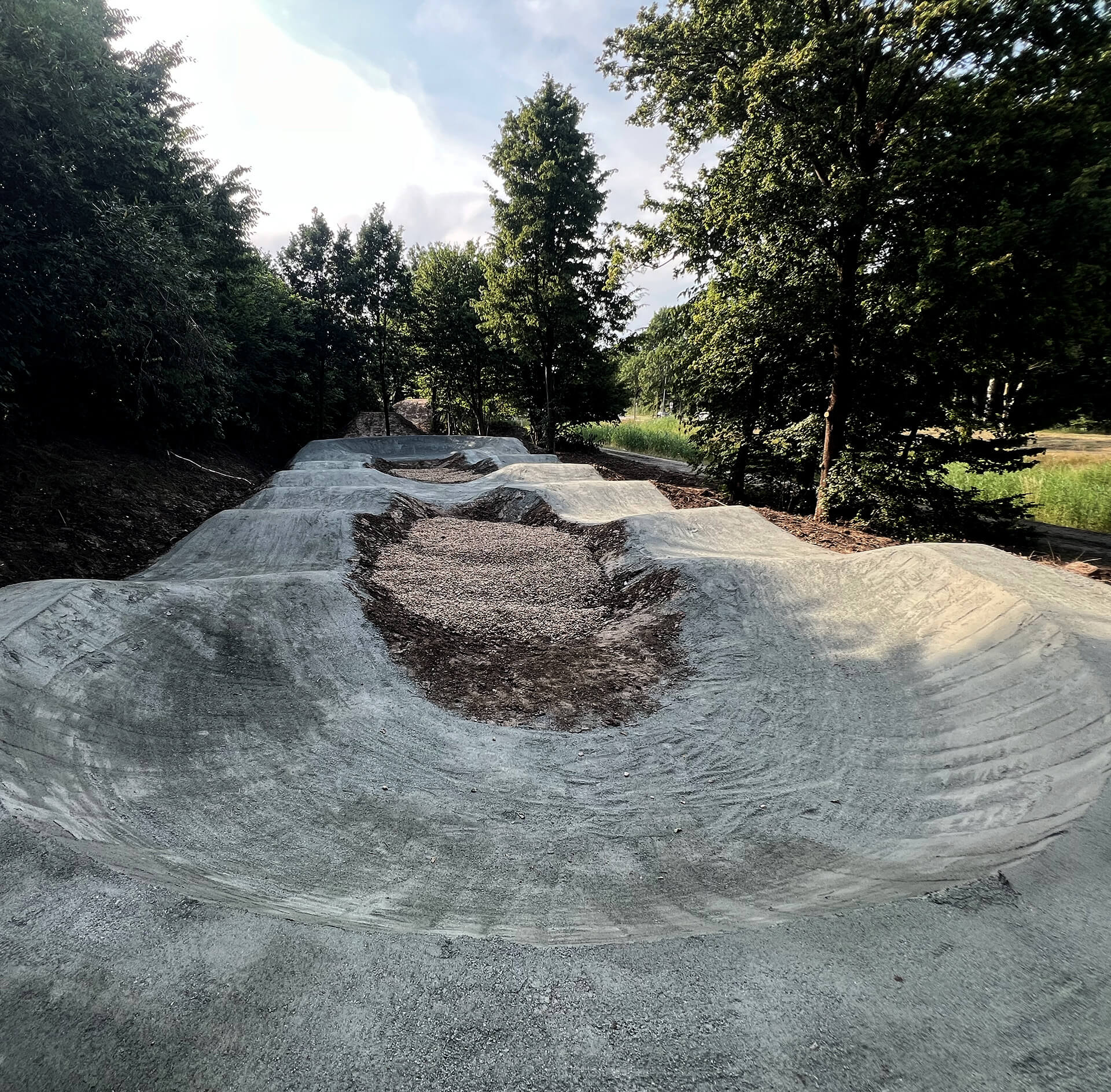 Pumptack with dirt and sand in a green area. A green tree on the right side