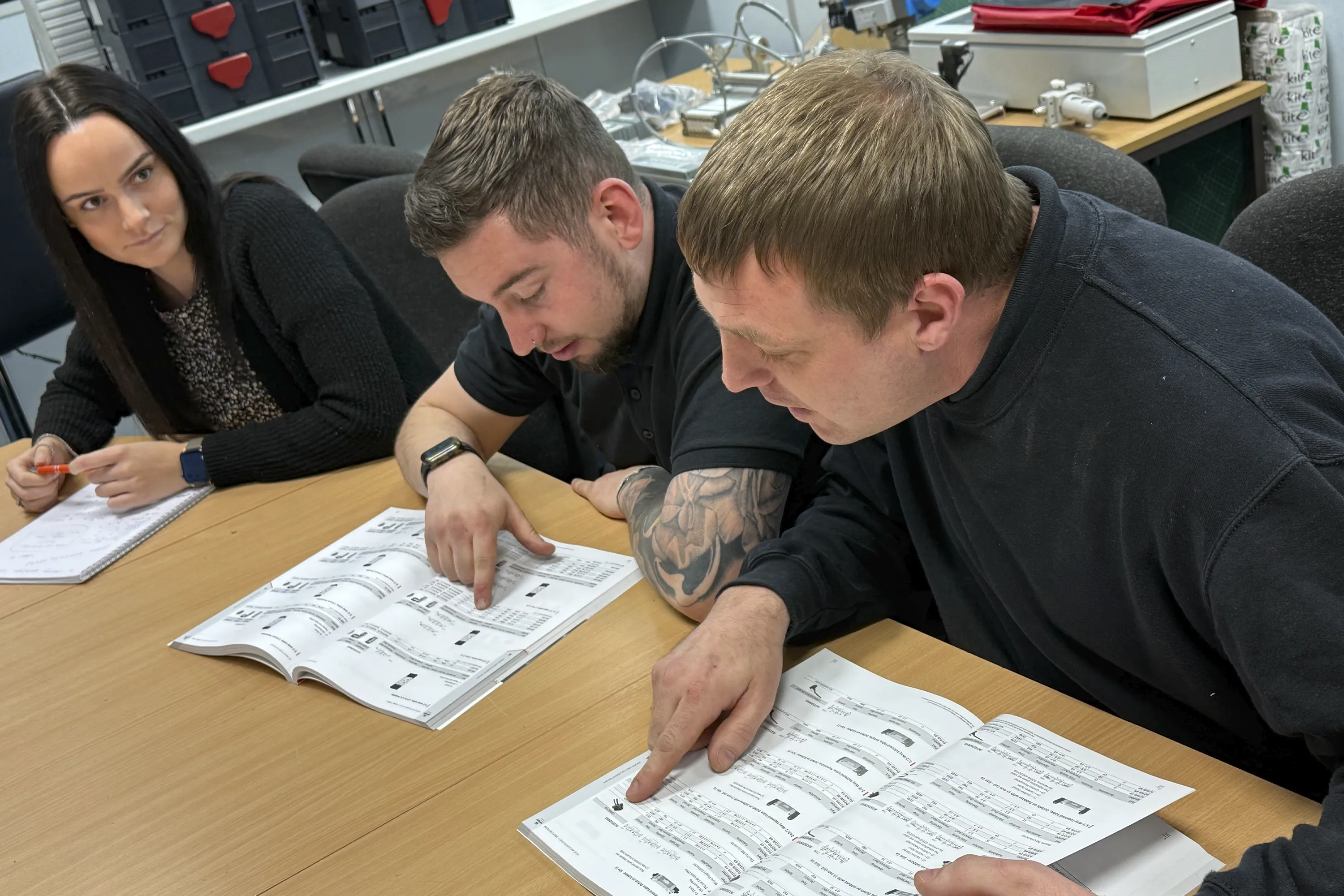 Three delegates working closely together at a desk, carefully studying open training manuals during our Introduction to Pneumatics course. They are pointing out specific ISO 1219 symbols and component specifications, highlighting the collaborative, hands-on environment that helps engineers and maintenance teams build genuine confidence before moving on to physical circuit builds