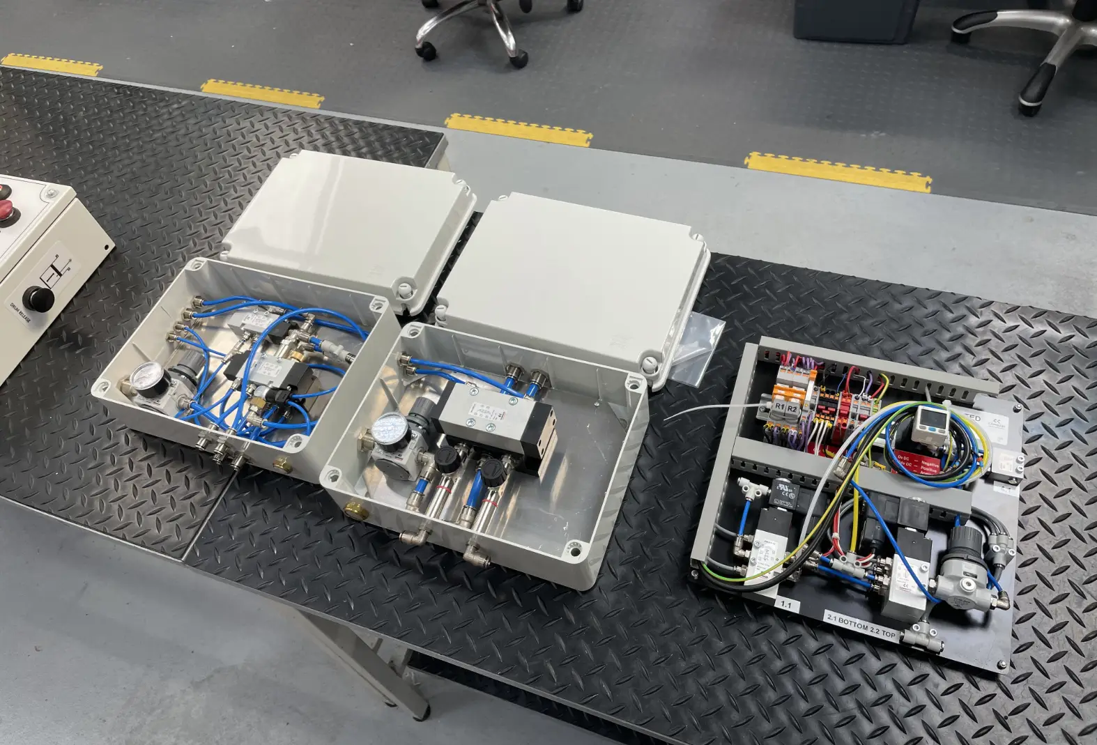 Three custom pneumatic and electro-pneumatic control panels, including IP-rated enclosures and wired baseplates, sitting on a workbench ready for testing at the UK Automation Centre.
