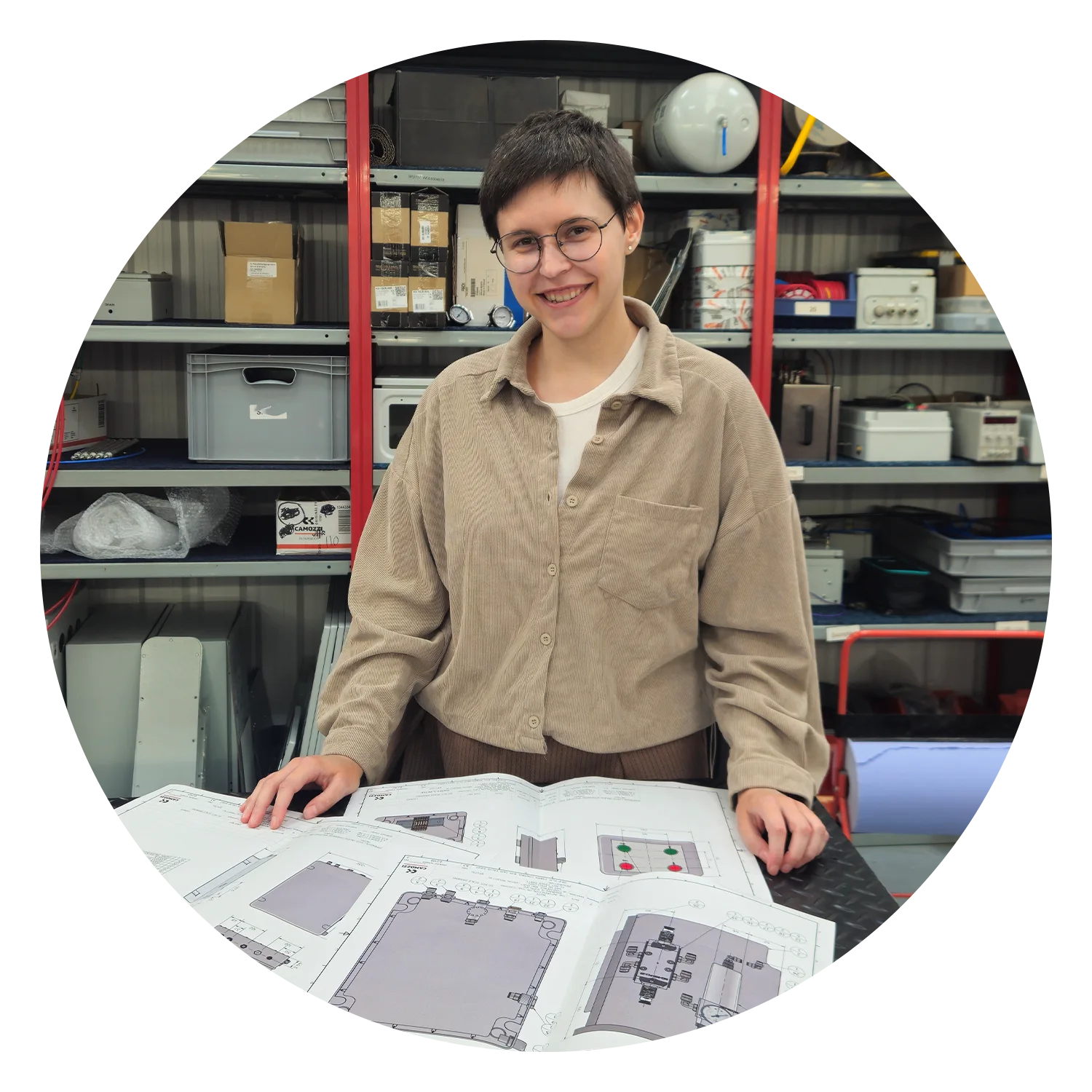 Alla, CAD Engineer at Camozzi Automation UK, smiling while reviewing printed 2D technical CAD drawings and pneumatic enclosure schematics on a workshop bench.