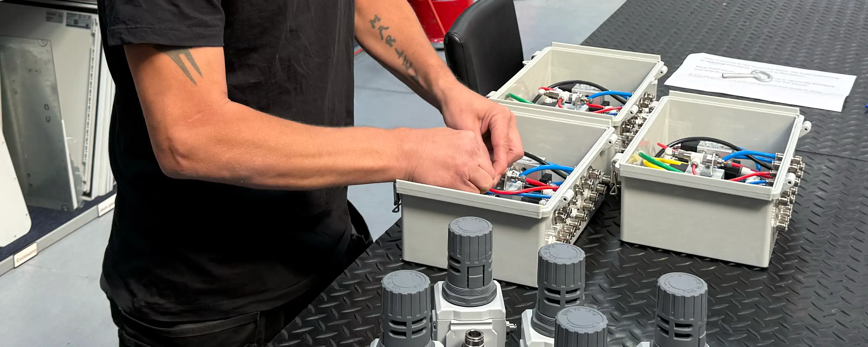 A Camozzi UK engineer assembling a batch of compact custom pneumatic control panels on a workbench, routing coloured tubing into grey enclosures alongside air preparation units.