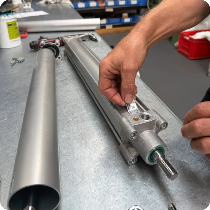 Close-up of a technician applying a scannable traceability label to a finished custom pneumatic cylinder, denoting its manufacturing date and engineer code for strict quality assurance.