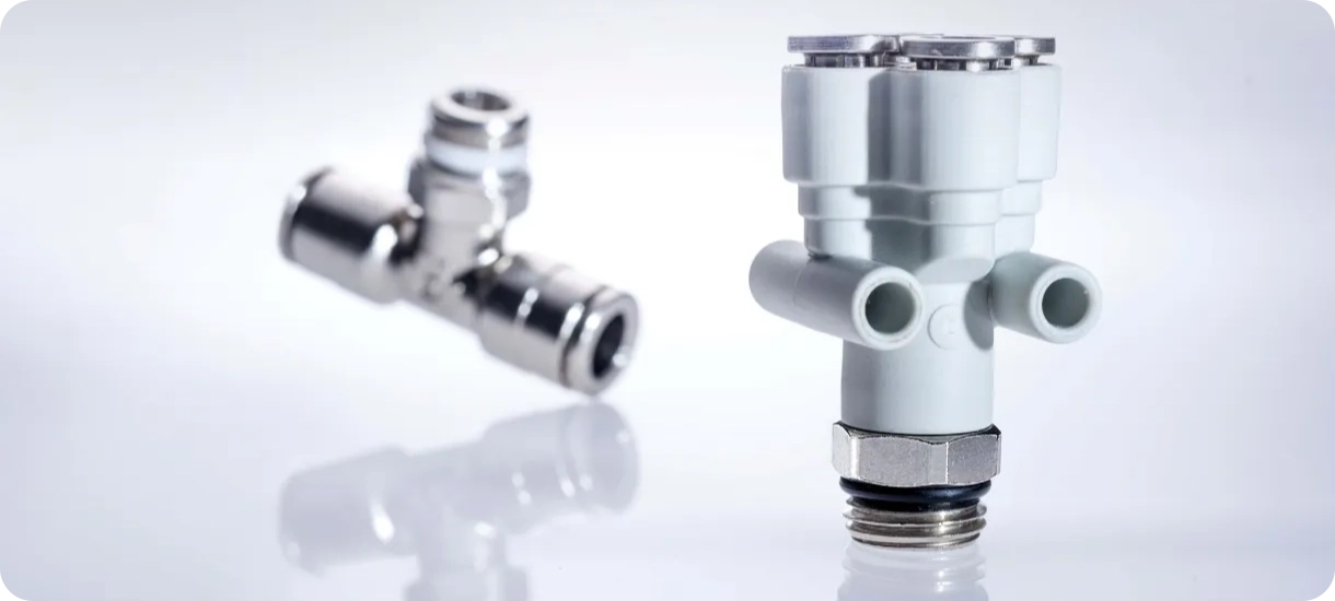 A metal tee push-in fitting alongside a multi-port technopolymer fitting, illustrating the range of shapes, materials and thread sizes required for secure pneumatic tubing connections.