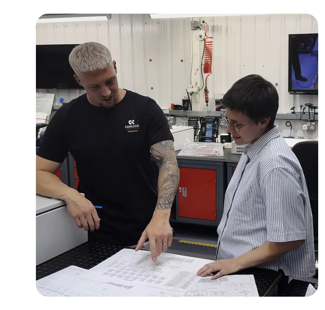 Two Camozzi UK engineers discussing and reviewing technical drawings on a workshop table, showcasing bespoke electro-pneumatic design collaboration.
