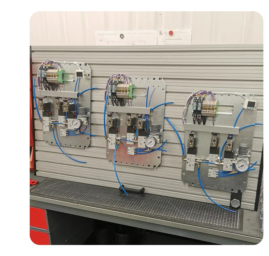 Three electro-pneumatic panel backplates mounted side-by-side on a slatted workshop testing rig, populated with terminals and solenoid manifolds connected for functional validation.