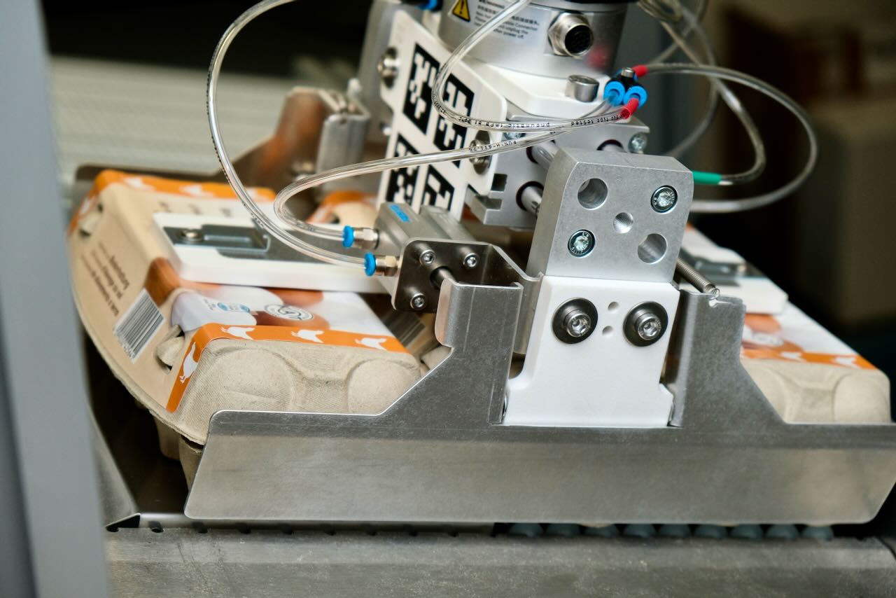 Pneumatic gripper grasping three egg cartons of 10 eggs simultaneously.