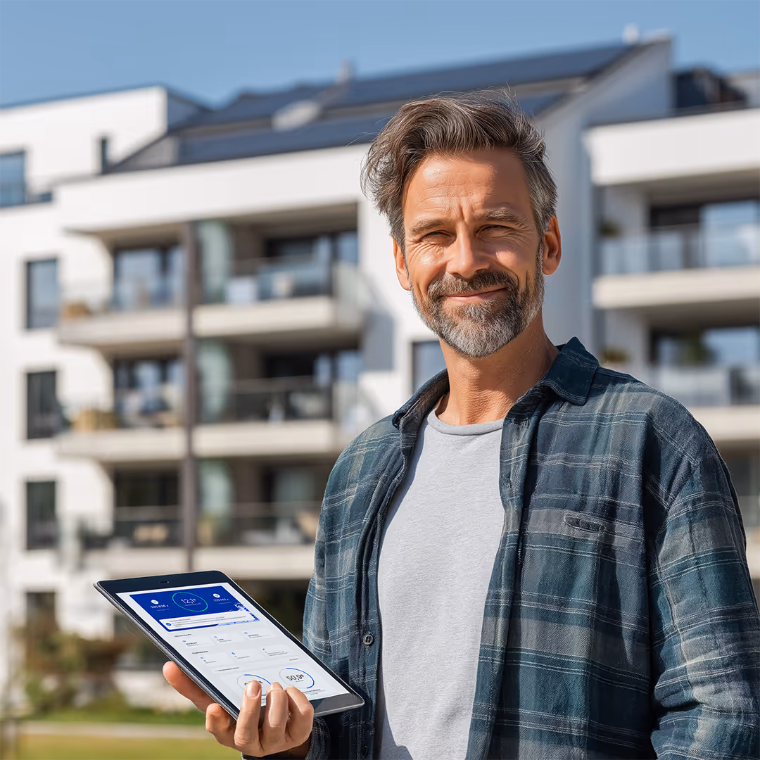 zufriedener metergrid Plus-Kunde vor seinem PV-Mehrfamilienhaus mit Tablet mit metergrid Software in der Hand