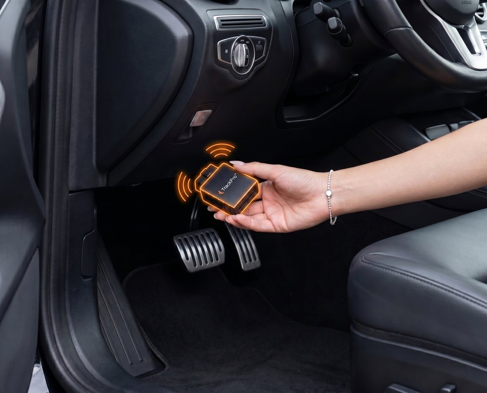Hand steckt den TrackPro FMC003 in die OBD-Buchse im Fußraum