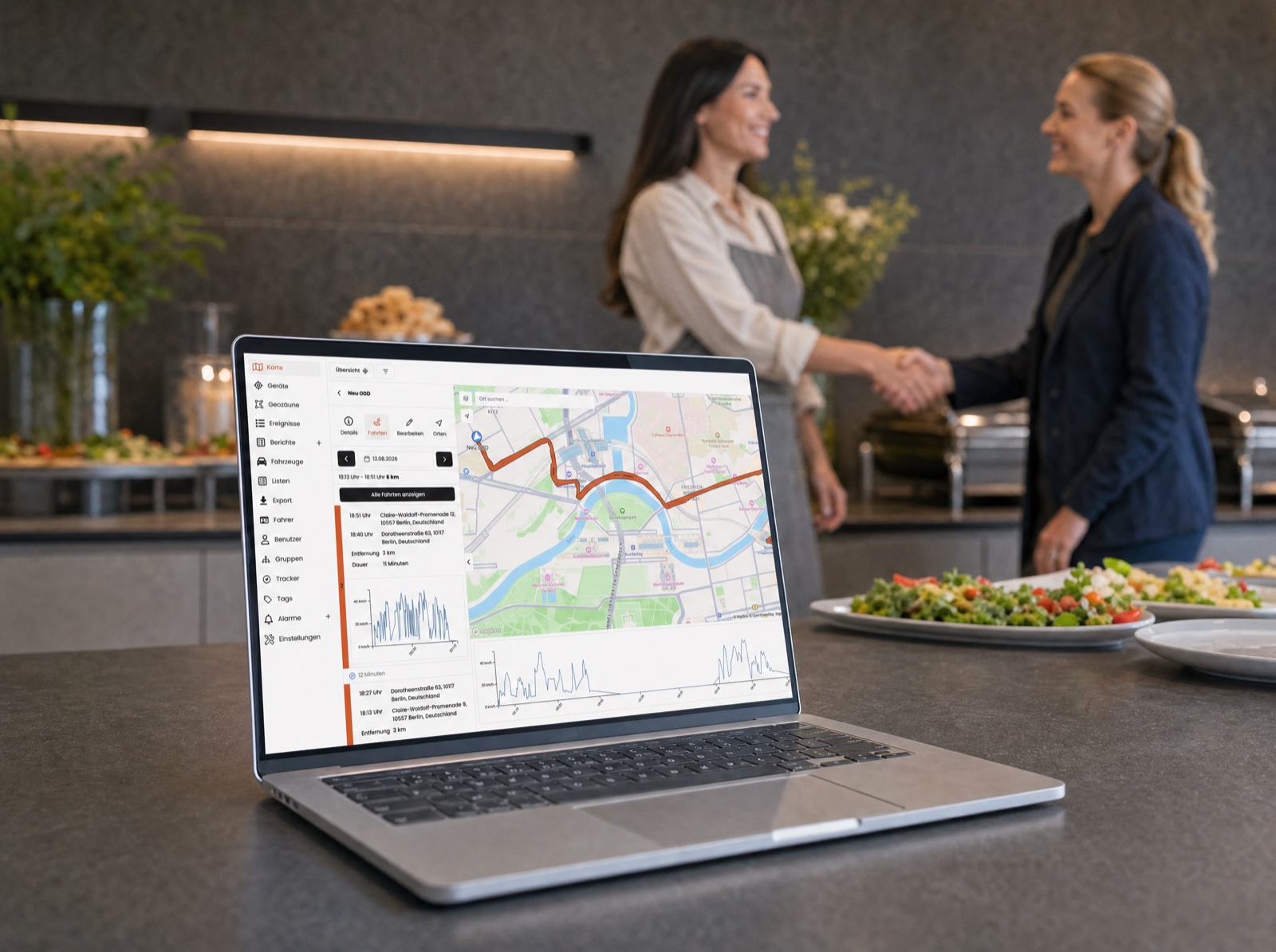 Laptop mit der TrackPro Fahrzeugübersicht, im Hintergrund ein Kundengespräch beim Catering