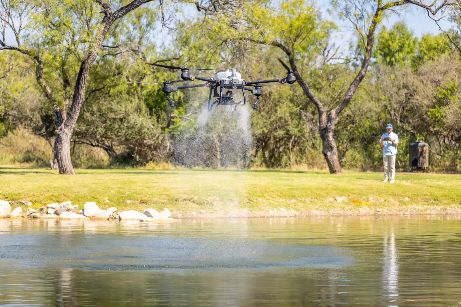 Agricultural drone applying seed and pond sealant over a Texas pond and pasture