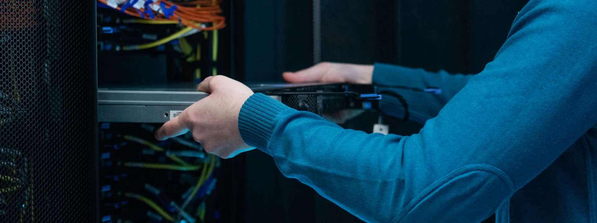 Person in blue sweater handling a server hard drive in a data center rack.