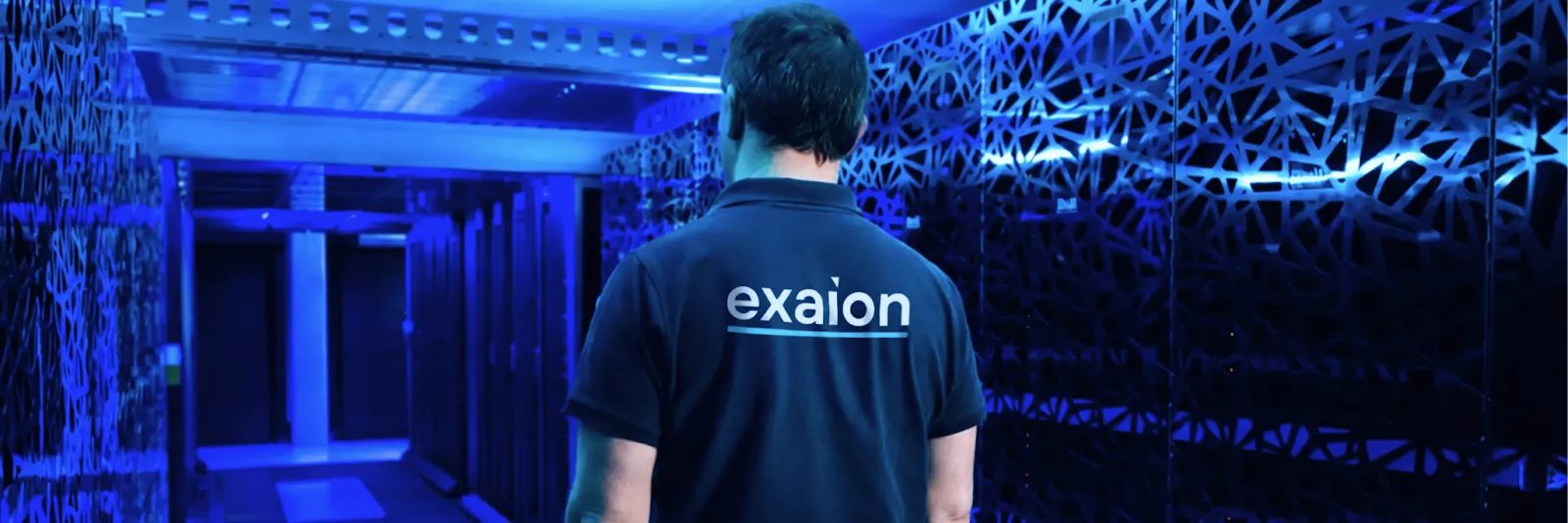 Person wearing a navy shirt with 'exaion' on back standing in a blue-lit tech corridor.
