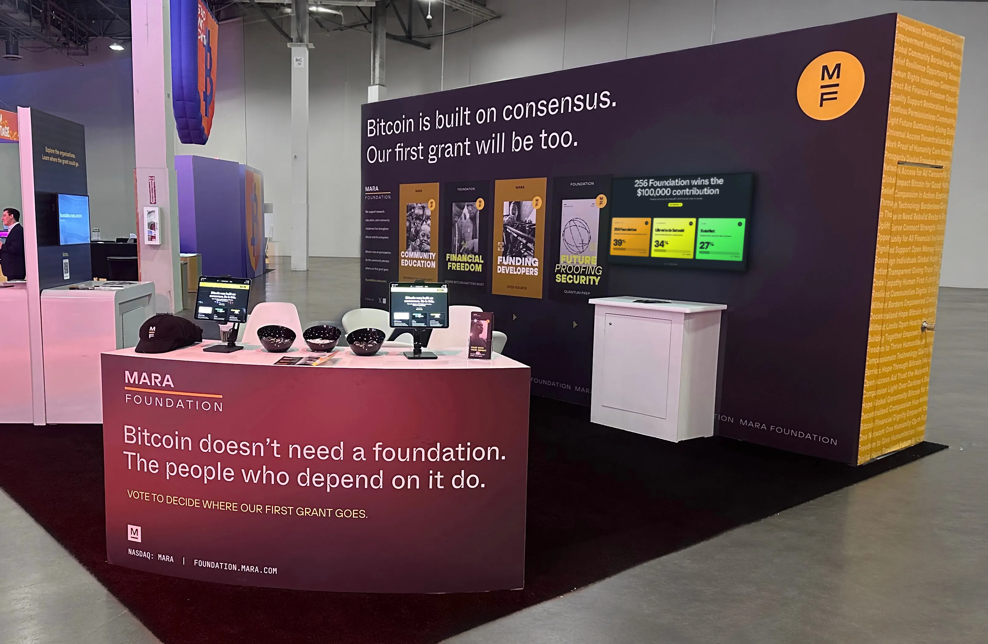 MARA Foundation booth with Bitcoin grant voting info and screens inside a convention hall.
