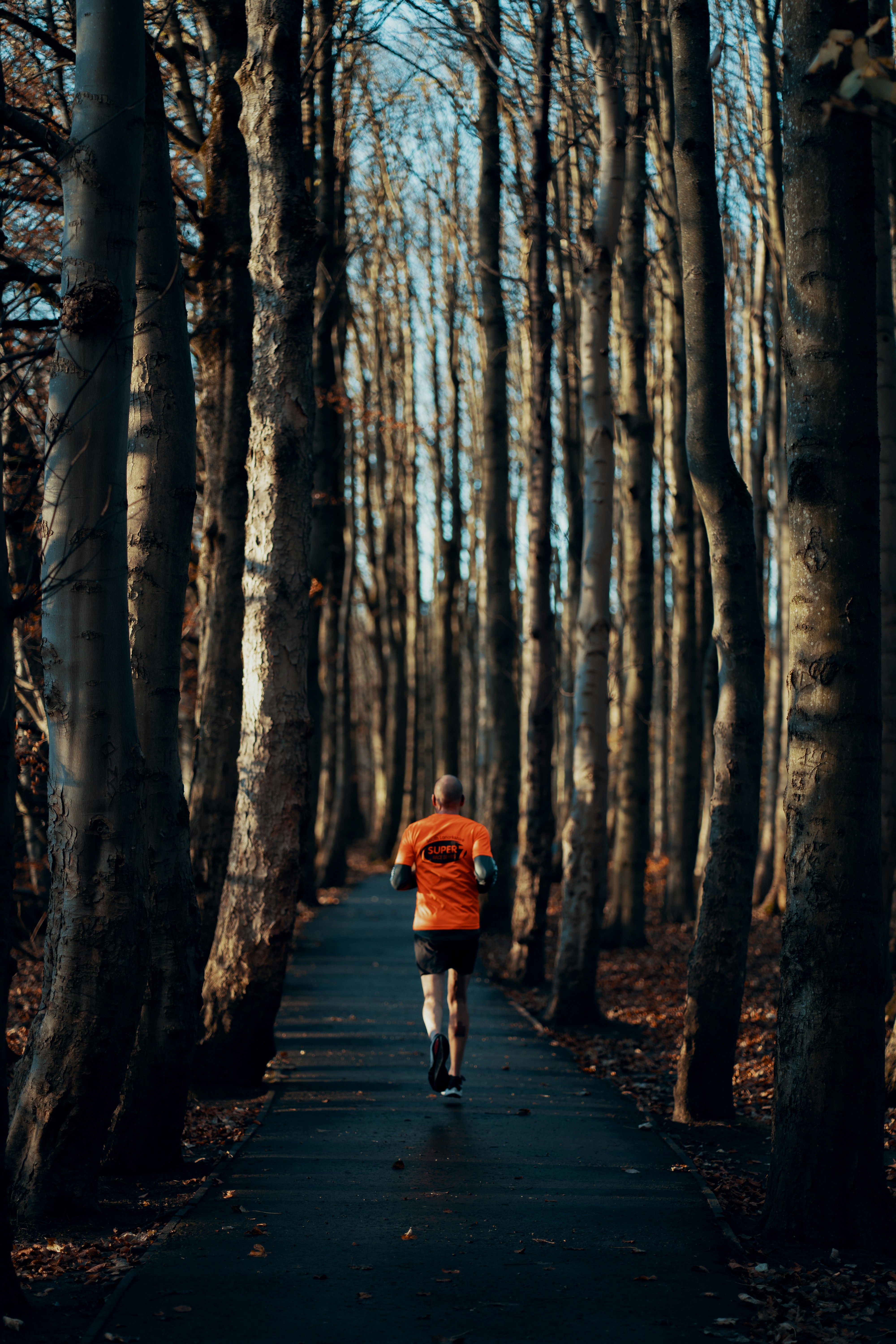 A person jogging in the woods wearing an orange shirt.