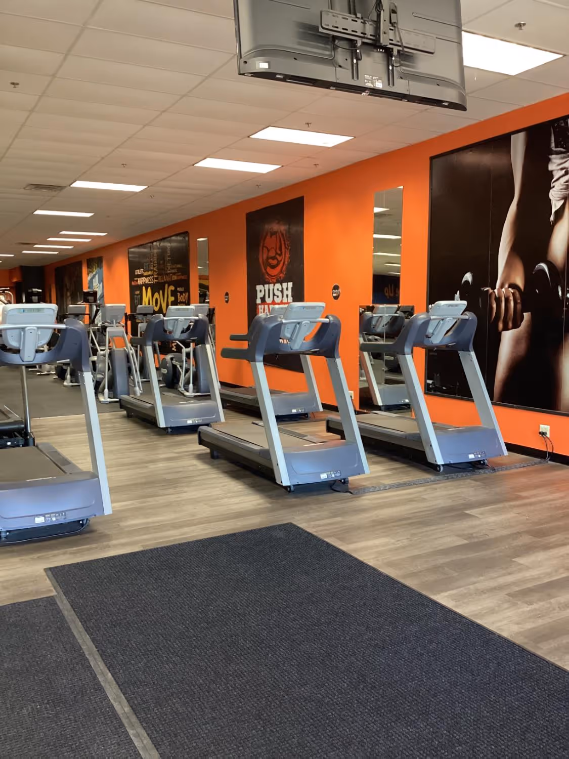 Row of treadmills in a gym with orange walls and motivational posters.