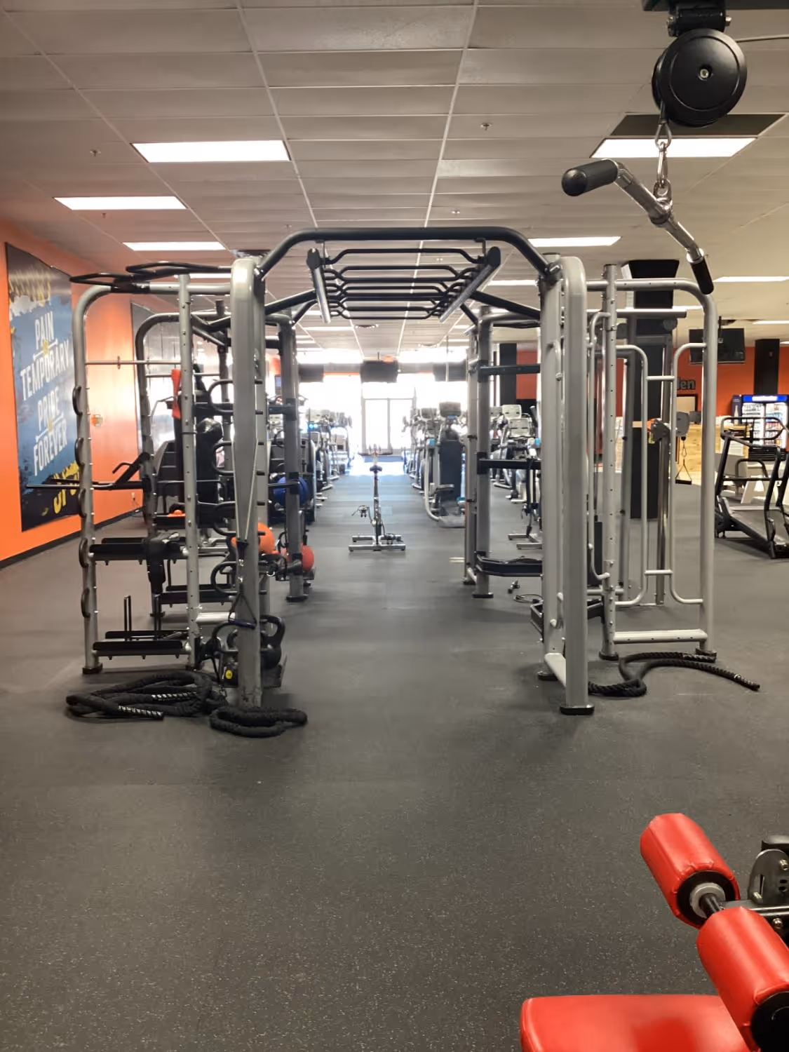 Interior of a gym with various exercise machines, weight racks, and cardio equipment lined up in rows.