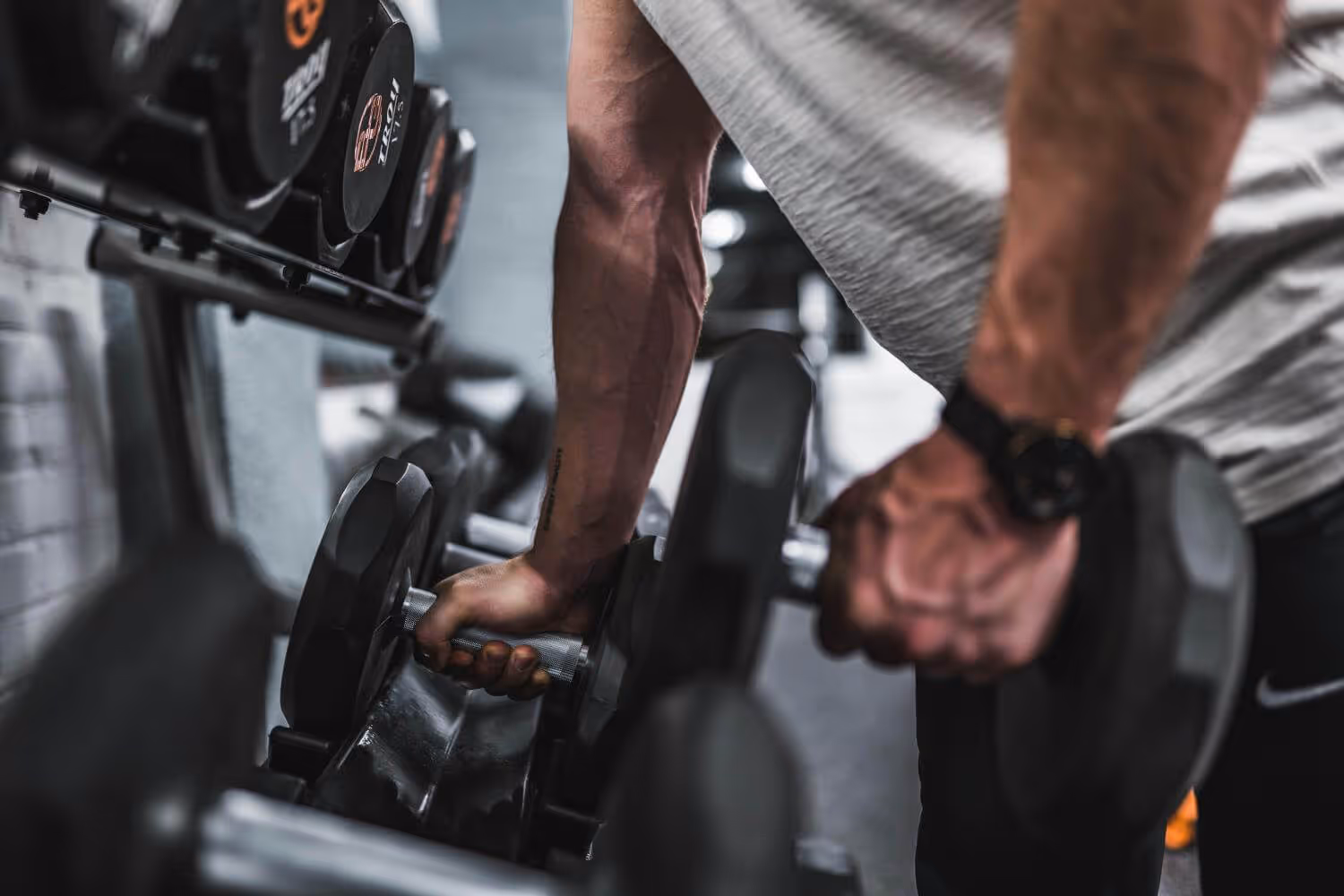 Close-up of a person gripping a dumbbell near a rack of weights in a gym.