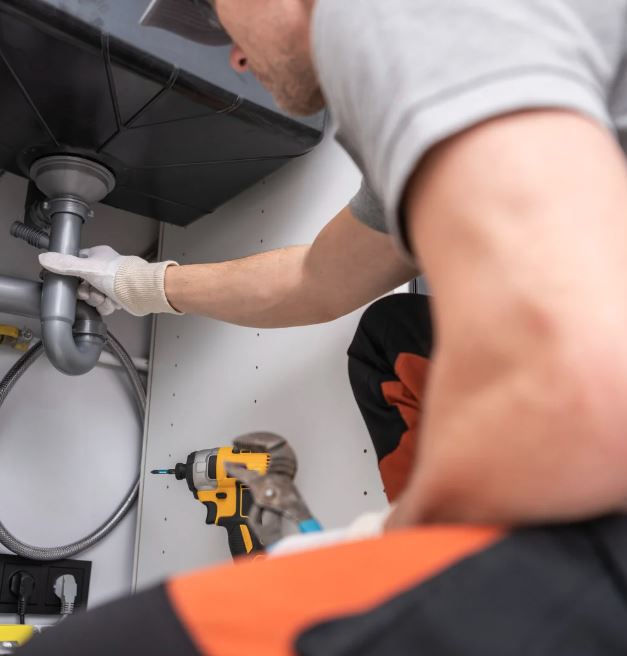 Plumber in San Diego CA performing drain cleaning under sink.