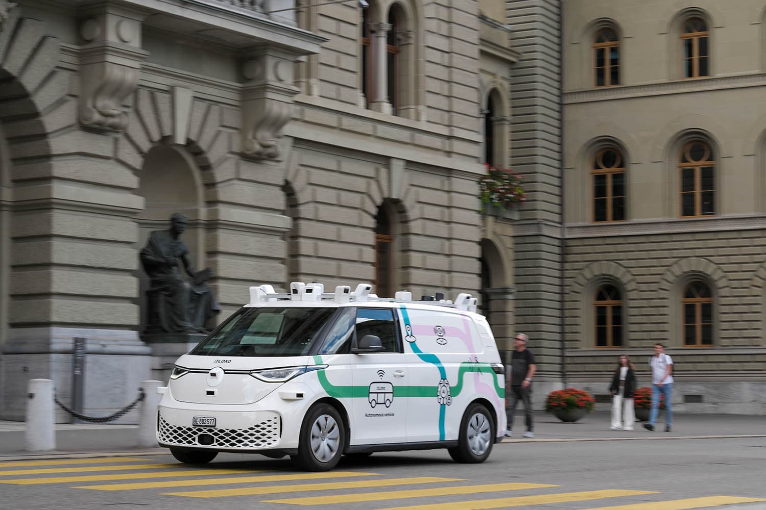 Autonomous shuttle driving through historic city center, surrounded by pedestrians and classic architecture.