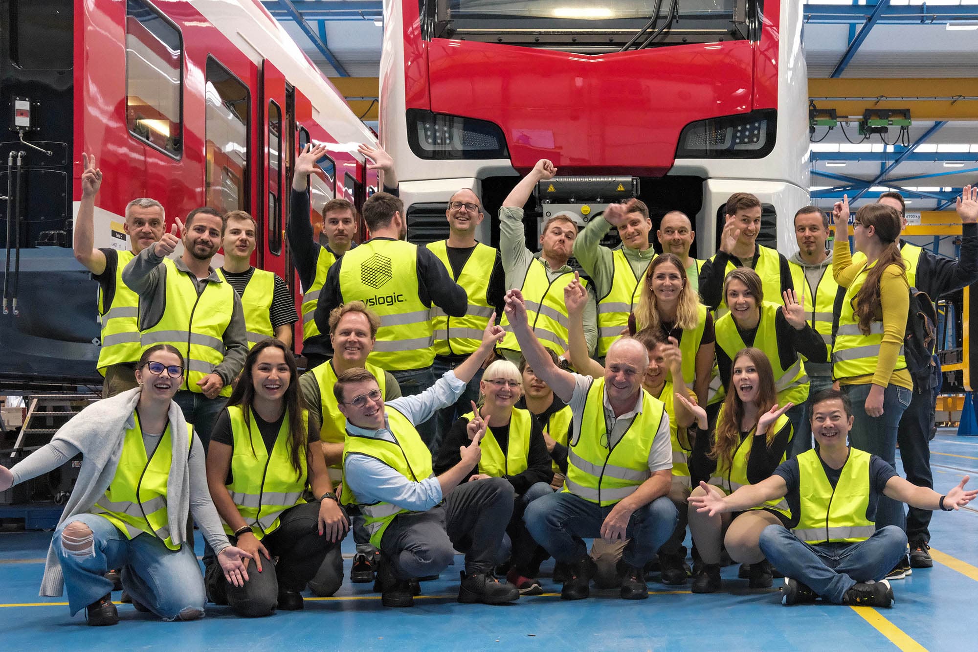 Syslogic employees posing cheerfully in Stadler Rail’s Bussnang production hall in front of a red train