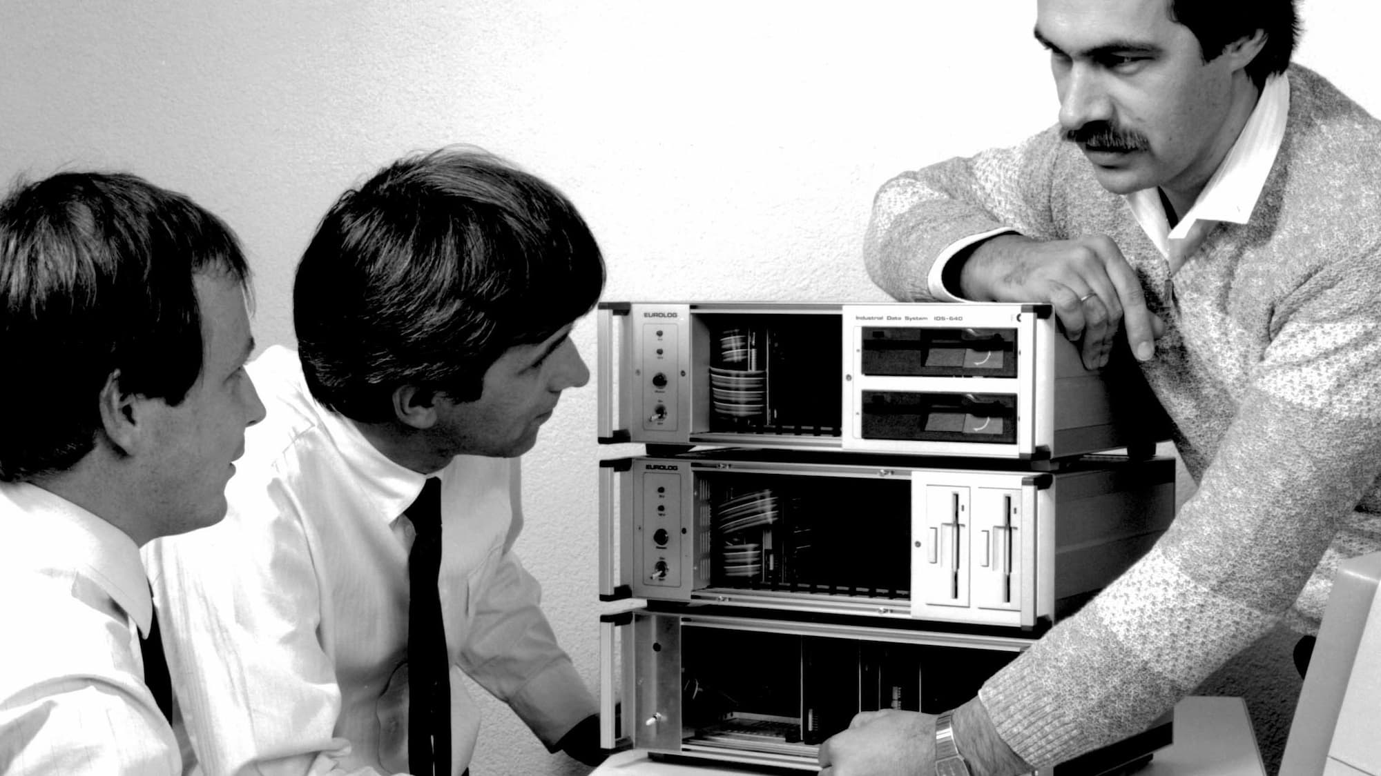 Historical photograph from Syslogic’s early years: Three engineers discussing hardware design at a desk.