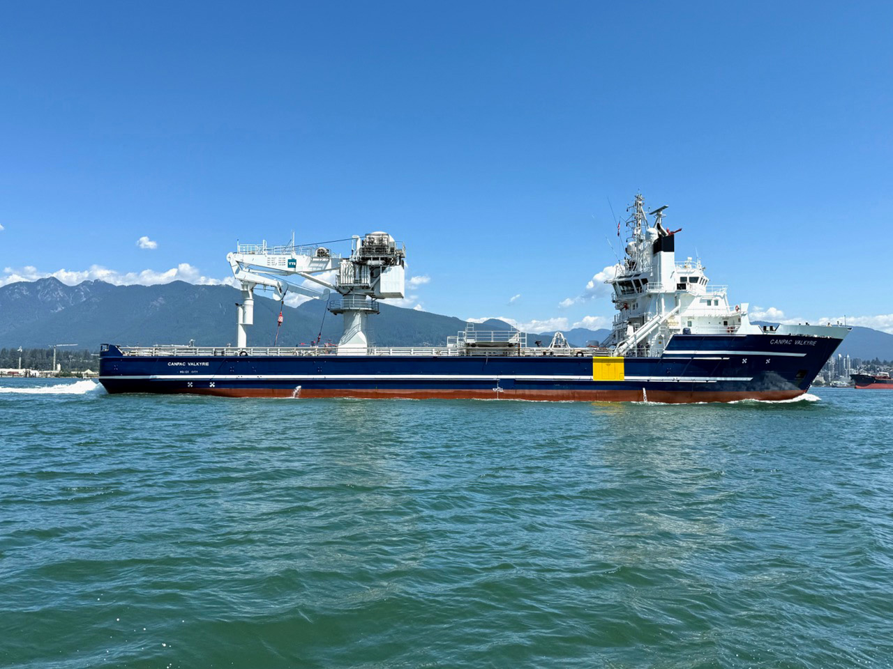 Offshore vessel Canpac Valkyrie underway, with mountains and the Vancouver coastline in the background.