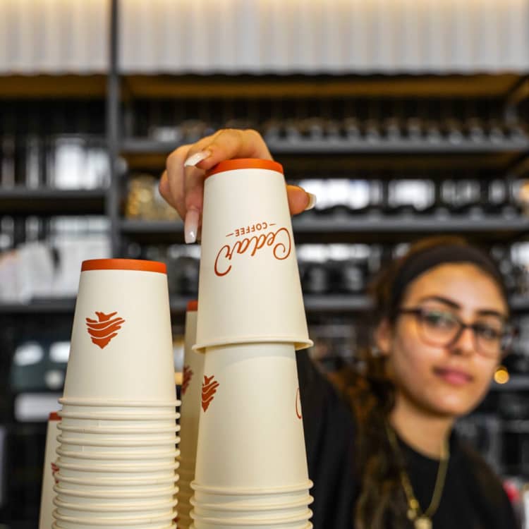 A cedar bakery barista reaching for a branded coffee cup