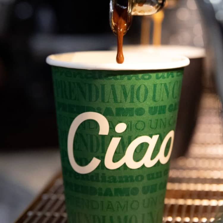 Printed coffedecup displaying the word 'Ciao' while being filled with fresh espresso coffee