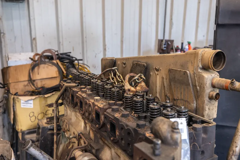Disassembled diesel engine cylinder head with valve springs exposed, showing signs of wear and grime.