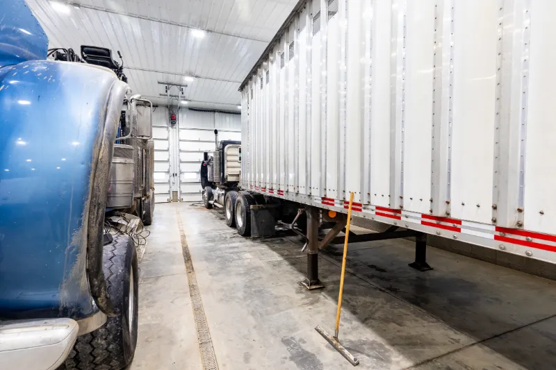 Heavy-duty trailer service in progress with a semi-trailer parked indoors beside a blue rig and floor squeegee.