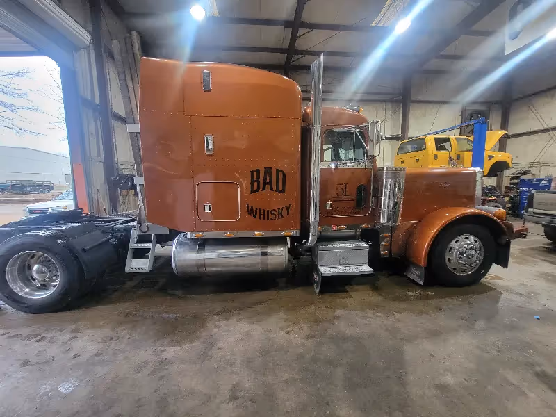 Heavy-duty truck repair on brown semi tractor in shop bay with “BAD WHISKY” and “5L” on cab.