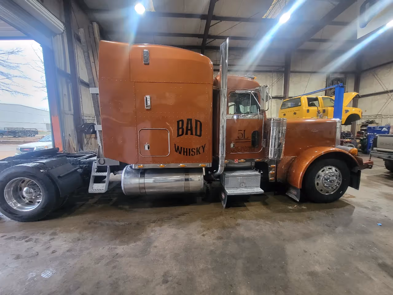 Heavy-duty truck repair on brown semi tractor in shop bay with “BAD WHISKY” and “5L” on cab.