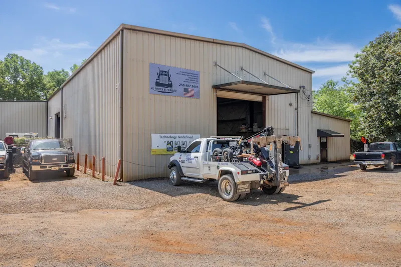 Heavy-duty truck repair facility with service bays, company signage reading "4L Truck & Trailer," and service vehicles outside.