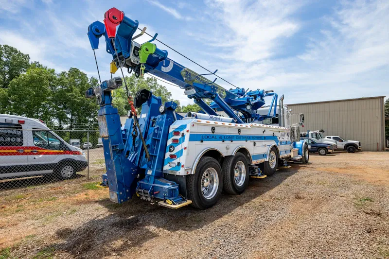 Roadside heavy-duty wrecker equipped for local and long-distance towing, parked outside a commercial repair facility. The truck displays "Local & Long Distance Towing."