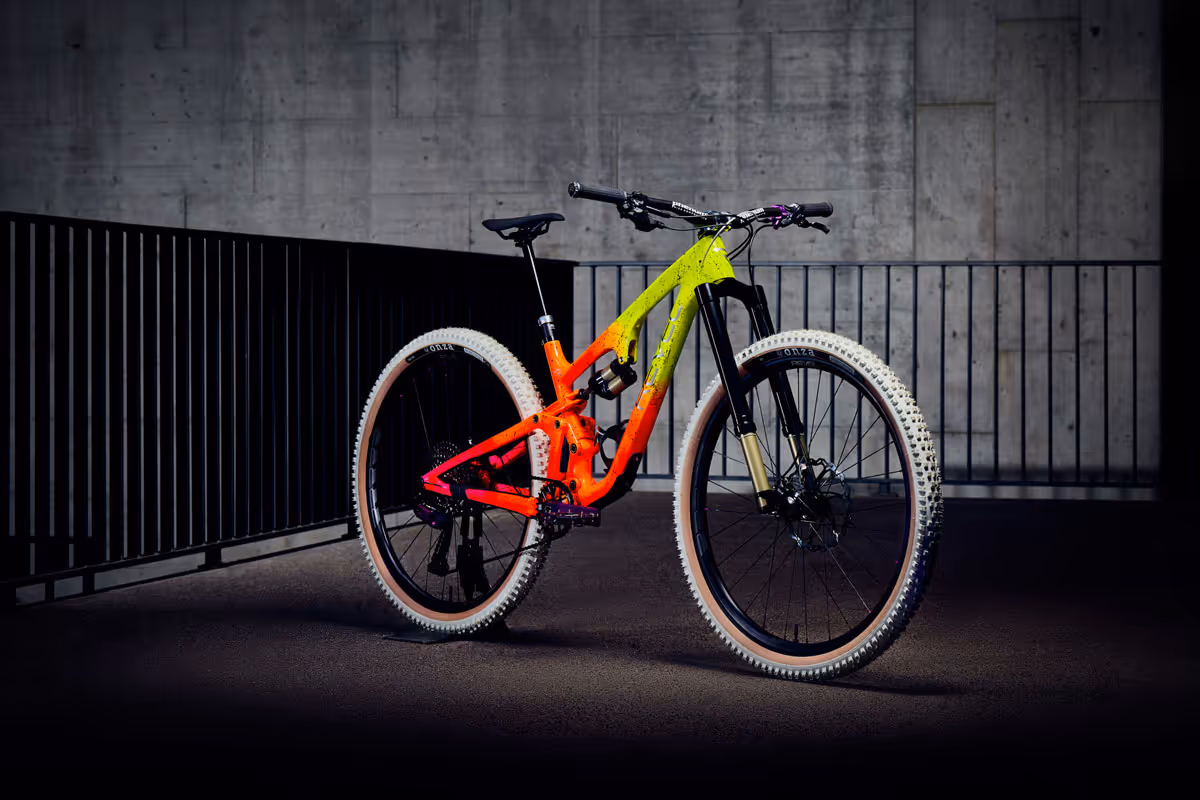 Mountainbike mit neongrünem und neonrotem Rahmen vor einer Betonwand und schwarzen Metallgeländern.