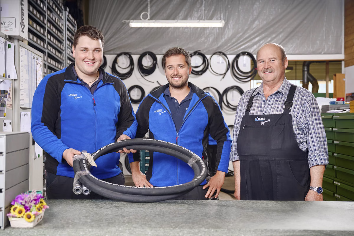 Drei Mitarbeiter mit Hydraulikschlauch in Werkstatt