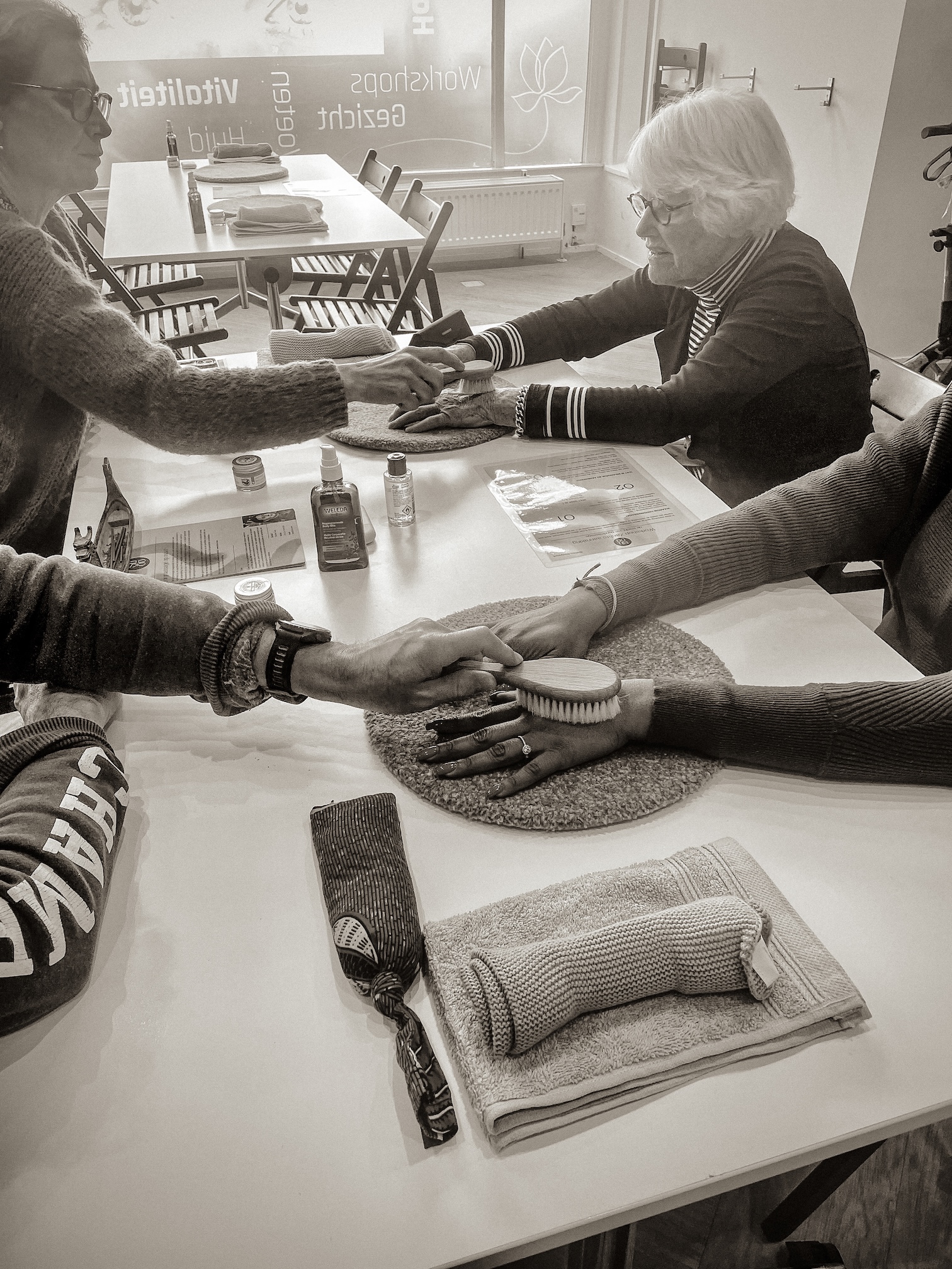Handen rond een tafel tijdens een handmassage-workshop voor mantelzorgers en zorgmedewerkers in een verzorgingshuis