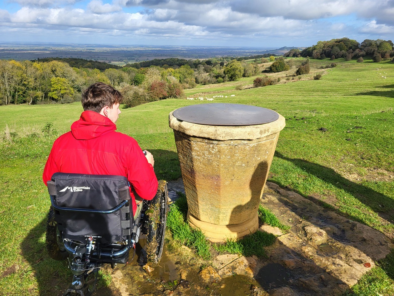 A young man in a wheelchair who is a member of Experience Community on the Cotswold Way national Trail at Dover's Hill, looks out over the Cotswolds towards the Severn Estuary