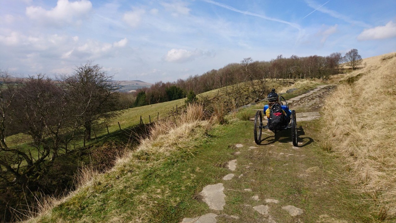 A man in a wheelchair tackles a rough trail that leads upwards on a section of the Pennine Bridleway National Trail