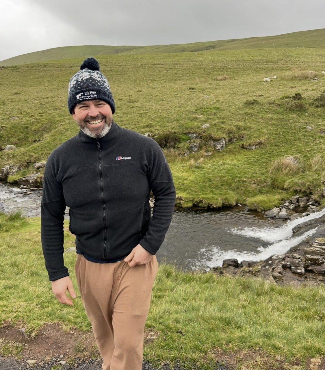 Gareth Davies wrapped up warm, wearing a fleece and bobble hat, smiling while walking the Pembrokeshire Coast Path National Trail